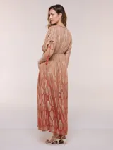 Vestido largo de gasa color salmón con un sutil patrón estampado brillante en tono dorado. Cuenta con escote en V cruzado, cintura imperio elastizada y mangas cortas con tiras ajustables terminadas en borlas.
