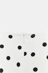 Top blanco con estampado de lunares negros, escote en pico, mangas sisa con hombreras, cintura con frunces laterales y cierre trasero con cremallera oculta.
