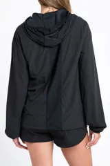 Campera deportiva de color negro con cierre frontal, capucha y mangas largas con puños elásticos. Presenta una textura ligera y un corte ajustado al cuerpo.