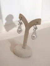 Caravanas colgantes de metal plateado con diseño de perlas de distintos tamaños, incluyendo perlas barrocas en la parte inferior.