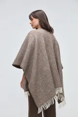 Ruana de lana sin teñir en tonos beige, con textura acanalada y terminaciones con flecos en los bordes.