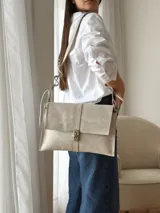 Bandolera de cuero color beige claro, con solapa frontal, cierre metálico de broche y correa regulable con detalles ondulados.