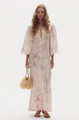 Vestido largo de lino con estampado floreado en tonos rosados, cuello camisero, botonadura frontal de nácar y mangas amplias abullonadas con puños elásticos. Presenta aberturas laterales en la falda.