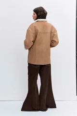 Cazadora de efecto piel en color tostado con interior y solapas de borreguillo blanco. Presenta cierre frontal con botones, bolsillos laterales y mangas largas con puños de borreguillo.