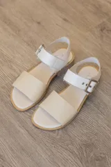 Sandalia plana de cuero color suela, con capellada lisa en la parte delantera y tira trasera con textura de reptil en tonos marrones y naranjas. Cuenta con una hebilla metálica grande en el tobillo y taco bajo.