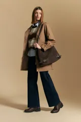 Cartera de gamuza negra con textura suave y acabado aterciopelado. Cuenta con una silueta amplia y flexible, cierre superior metálico, correa regulable y detalles laterales con hebillas.