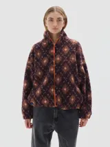 Campera de sherpa con estampado geométrico de rombos en tonos marrones y rosados. Presenta cuello alto, cierre frontal completo en color naranja vibrante y mangas largas con diseño holgado.