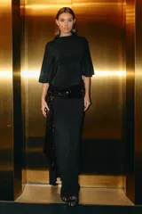 Vestido midi de color negro con cuello subido, mangas cortas amplias y espalda descubierta. Presenta un fajín integrado con aplicación de lentejuelas a tono y una abertura lateral en el bajo.