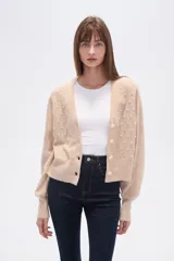 Cárdigan color beige de poliéster con cuello en V, corte al cuerpo y mangas abullonadas. Decorado con cuentas blancas.
