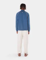 Campera deportiva estilo track jacket, color azul con franjas laterales en color salmón. Posee cuello alto, cierre frontal y bolsillos laterales.