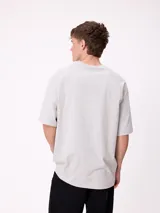 Remera de corte holgado color gris melange, con mangas raglán y estampado frontal con el logo de la marca Rusty en tonos azul y rojo.