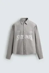 Camisa de corte boxy fit confeccionada en tejido de algodón con diseño de rayas verticales. Presenta cuello solapa, manga larga con puños abotonados y cierre frontal de botones. El frente destaca por bordados y estampados a contraste.