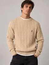 Sweater tejido de punto con diseño de trenzas, color beige, con cuello redondo y detalles de rib en cuello, puños y dobladillo. Presenta un pequeño bordado en el pecho.