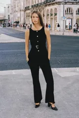 Chaleco negro de vestir, sin mangas, con cuello redondo y cierre frontal de botones metálicos dorados. Incluye dos bolsillos frontales con solapa y un cinturón negro a tono con hebilla metálica dorada.