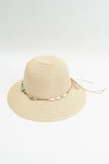 Sombrero de ala ancha color beige, confeccionado en material tejido tipo paja. Presenta un cordón decorativo alrededor de la copa con cuentas de madera, piedras turquesas y detalles metálicos.