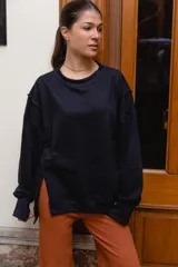 Buzo negro de felpa con diseño oversize, cuello redondo ribeteado y aberturas laterales en el dobladillo. Mangas largas con costuras caídas y puños anchos.