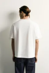 Camiseta relaxed fit color blanco, de cuello redondo y manga corta. Presenta un pequeño parche aplicado a contraste en el extremo de la manga y terminaciones en rib.