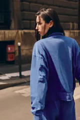 Chaqueta azul de algodón con cuello alto, cierre frontal de cremallera, bolsillos laterales y mangas largas con puños elásticos.
