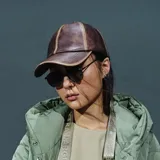 Gorra tipo béisbol confeccionada en cuero sintético color marrón con efecto desgastado y costuras decorativas en contraste.