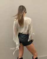 Camisa de manga larga acampanada, confeccionada en tejido satinado color beige, con diseño cruzado y tiras para anudar en la parte frontal.