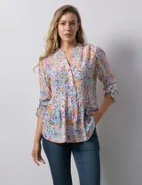 Blusa de gasa estampada con flores en tonos rosa, amarillo y azul. Tiene cuello a la base, escote en V y botones. La delantera tiene detalle plisado y las mangas son 3/4 regulables con presilla y botón.