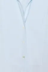 Camisa de popelín confeccionada en algodón, con cuello solapa, escote en pico y cierre frontal con botones. Presenta mangas largas con puños y un bajo redondeado asimétrico.