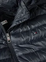 Campera acolchada azul marino de poliéster reciclado, con capucha y cierre de cremallera. Tiene dos bolsillos laterales con cremallera, es repelente al agua y presenta el logo de Tommy Hilfiger bordado en el pecho.