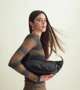 Cartera tipo medialuna de cuero brillante, con cierre de cremallera superior y correa extraíble con herrajes dorados.
