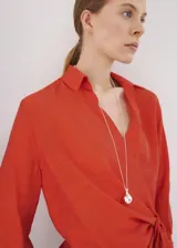 Camisa de viscosa y poliamida color rojo, con cuello camisero, manga larga y diseño cruzado con lazo ajustable en la cintura.