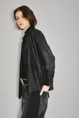 Camisa de cuero ovino color verde oliva, con cuello clásico, cierre frontal con botones y mangas largas con puños abotonados. Presenta un corte holgado y diseño tipo sobrecamisa.