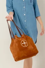 Bolso tipo tote bag de gamuza azul con asas de cuero marrón y bolsillo externo con logo bordado.