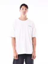 Remera blanca de corte oversize, con cuello redondo y manga corta. Presenta un pequeño estampado en el pecho con texto en color oscuro.