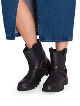 Bota corta de cuero color negro, con suela track de goma, puntera redonda y trabillas laterales. Cuenta con una correa decorativa alrededor del tobillo con textura símil serpiente y hebilla metálica.