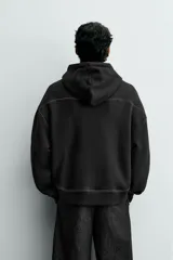 Sudadera tipo hoodie de corte relajado, color negro, con interior perchado. Presenta capucha ajustable con cordones en color crudo, bolsillo frontal tipo canguro y costuras a contraste en color blanco. Posee puños y ruedo en rib.