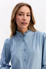 Blusa de algodón en color celeste, con textura sutil, cuello con volados y mangas largas con puños también decorados con volados. Presenta cierre frontal con botones.