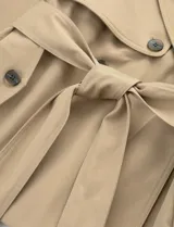 Gabardina corta de color beige, con diseño de doble botonadura, solapas anchas y cinturón ajustable en la cintura. Presenta bolsillos laterales y mangas largas.