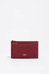 Billetera de estructura blanda confeccionada en nylon negro, con cierre de cremallera superior y bolsillo frontal con cierre. Presenta logo metálico dorado en el frente.