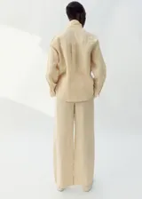 Pantalón de lino color beige, de diseño recto y largo con tiro medio, dos bolsillos laterales y cintura ajustable.