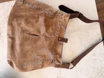 Cartera tipo hobo o de hombro de cuero color camel con efecto gastado. Presenta costuras decorativas en contraste color celeste y un anillo metálico dorado en el frente. Incluye correa ajustable de cuero marrón oscuro con hebilla dorada.