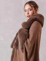 Ruana de tejido color tostado con cuello, bordes frontales y puños amplios con apliques de piel sintética al tono. Presenta una abertura central con cierre de botón tipo trenca.