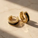 Par de caravanas tipo argolla de acero dorado con una franja central de esmalte negro.
