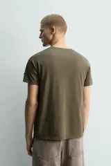 Camiseta de algodón color verde oliva, corte regular fit, con cuello redondo y manga corta. Presenta un pequeño corazón bordado en la manga.