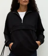 Buzo de modal color negro, con corte oversize, cuello alto con cierre frontal, mangas largas y recortes estructurados en el cuerpo.