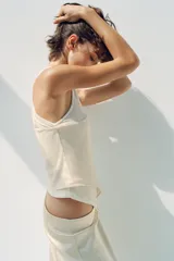 Camiseta sin mangas con diseño de doble capa y efecto choker incorporado al cuello. Presenta un corte asimétrico en el bajo y tiras decorativas caídas en un lateral.
