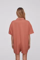 Mono corto color naranja, con cuello camisero, mangas cortas y cierre frontal con botones.