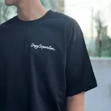 Remera de manga corta color beige natural, corte relajado, con un gran estampado gráfico en la espalda que incluye texto en negro y un diseño central de alas estilizadas en color rojo oscuro.