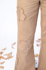 Pantalón largo color beige con parches en forma de flor con bordes desflecados.