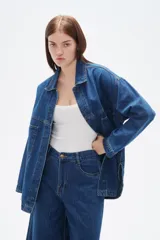 Sobrecamisa de jean azul oscuro, con corte holgado, cuello clásico, cierre frontal con botones metálicos y bolsillos laterales.