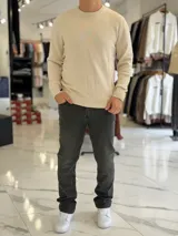 Buzo de hilo color beige claro, con cuello redondo y diseño clásico de manga larga.