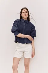 Camisa azul marino de cuello clásico, mangas abullonadas a tres cuartos y detalle fruncido en el frente. Presenta una silueta amplia y diseño corto con vuelo en el ruedo.